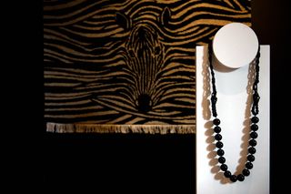 Black beaded necklace on display with a zebra print fabric hanging behind. Photographeds against a black background