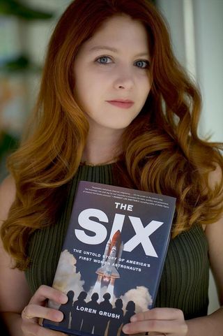 a woman with red hair holds a book.