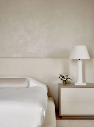 A white and cream bedroom with a textured beige wall, beige headboard and silk sheets