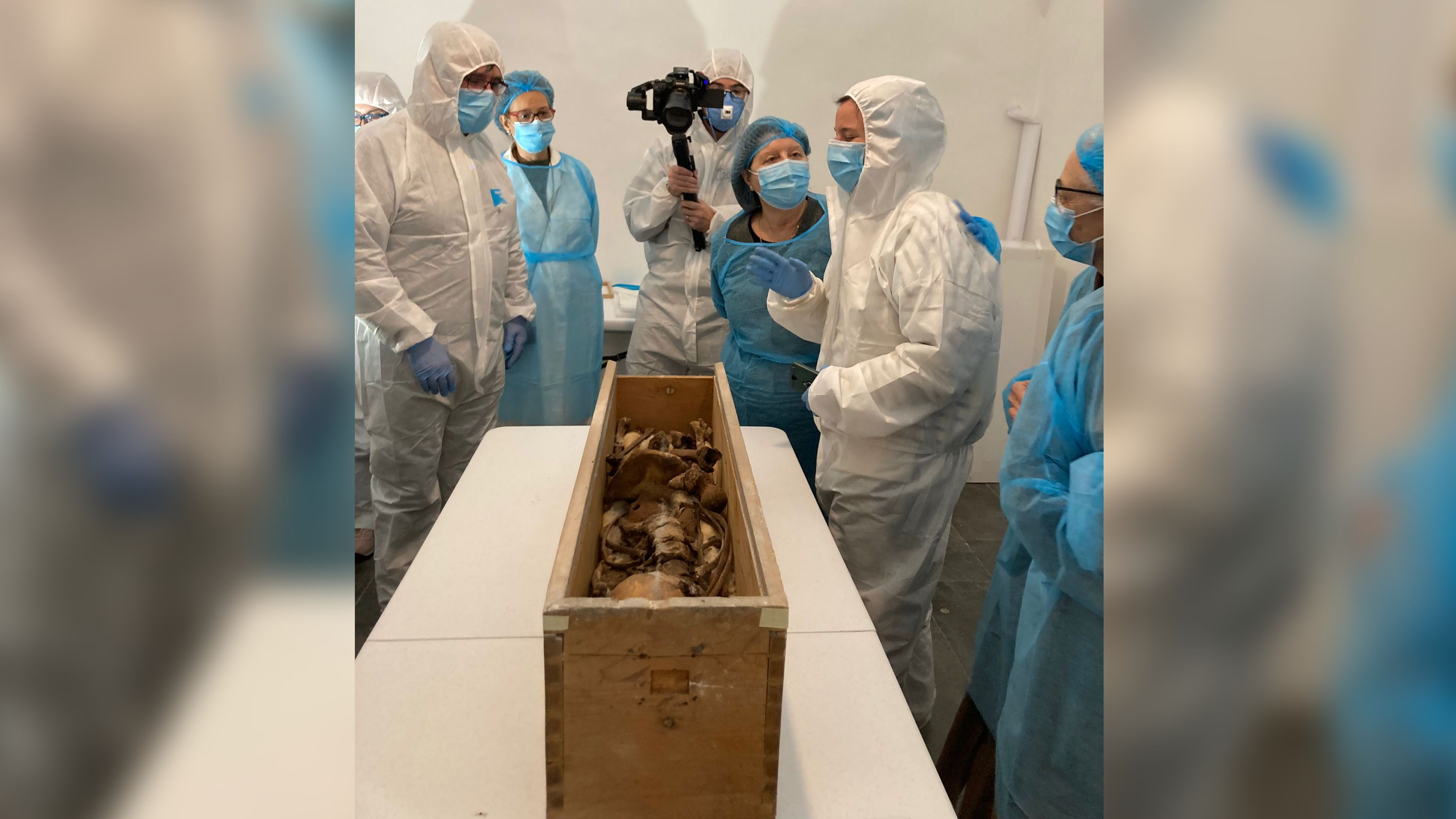 people standing around in PPE with a wooden box of human bones
