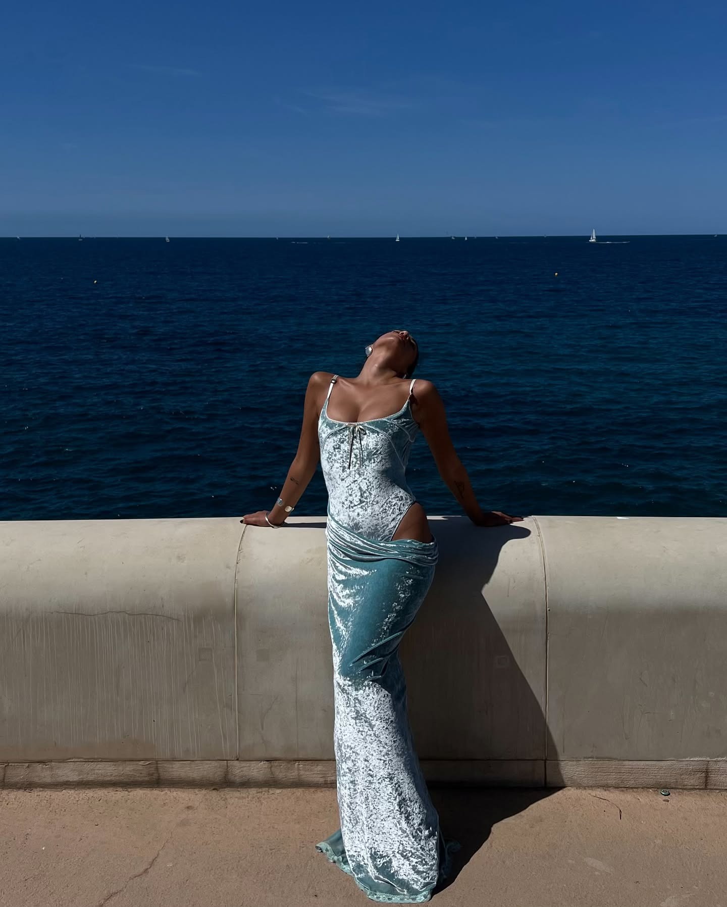 Woman wearing a crushed blue velvet swimsuit and maxi skirt against a deep blue sea.