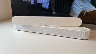 A white Sonos Beam Gen 2 soundbar photographed with the Sonos Ray on top and an OLED TV in the background