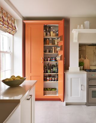 orange painted freestanding kitchen pantry, white kitchen, colourful blind, stone floor