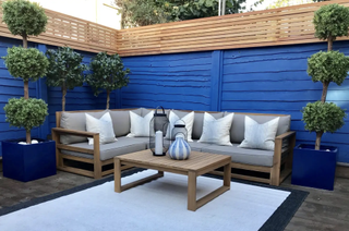 Low maintenance decking area in azur blue with L-shaped grey sofa and wooden table