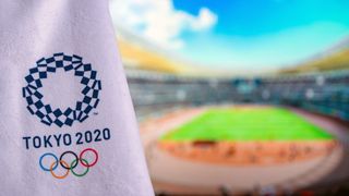 Hvidt Tokyo 2020 flag med olympiske ringe. Atletikstadion i baggrundenthletics stadium in background