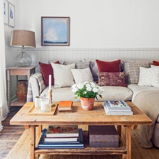 a living room with a beige sofa and a selection of beige, cream and red/pink cushions and wooden coffee table