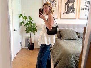 Stylist and fashion editor Natalie Cantell taking a mirror selfie wearing Stella McCartney denim, a white flowy summer top, and a black Celine Croque shoulder bag.