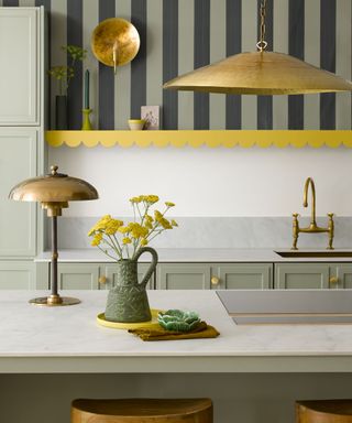 Kitchen shelves lined with scalloped edging painted yellow beneath striped wallpaper