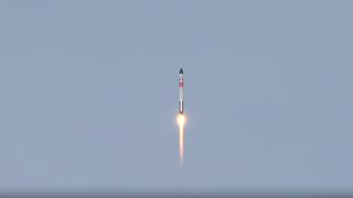 a white, black and red rocket lab electron rocket launches into a blue sky.