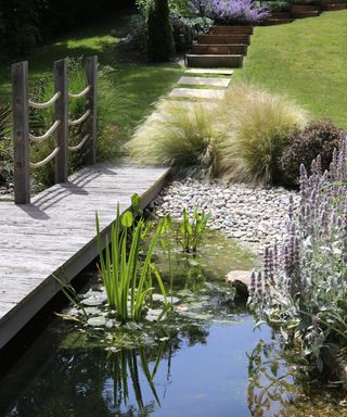 A naturally designed water feature with a wooden walkway bridge leading into a path