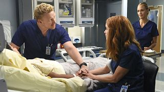 Owen, Megan and Teddy stand around Farouk's hospital bed on Grey's Anatomy.