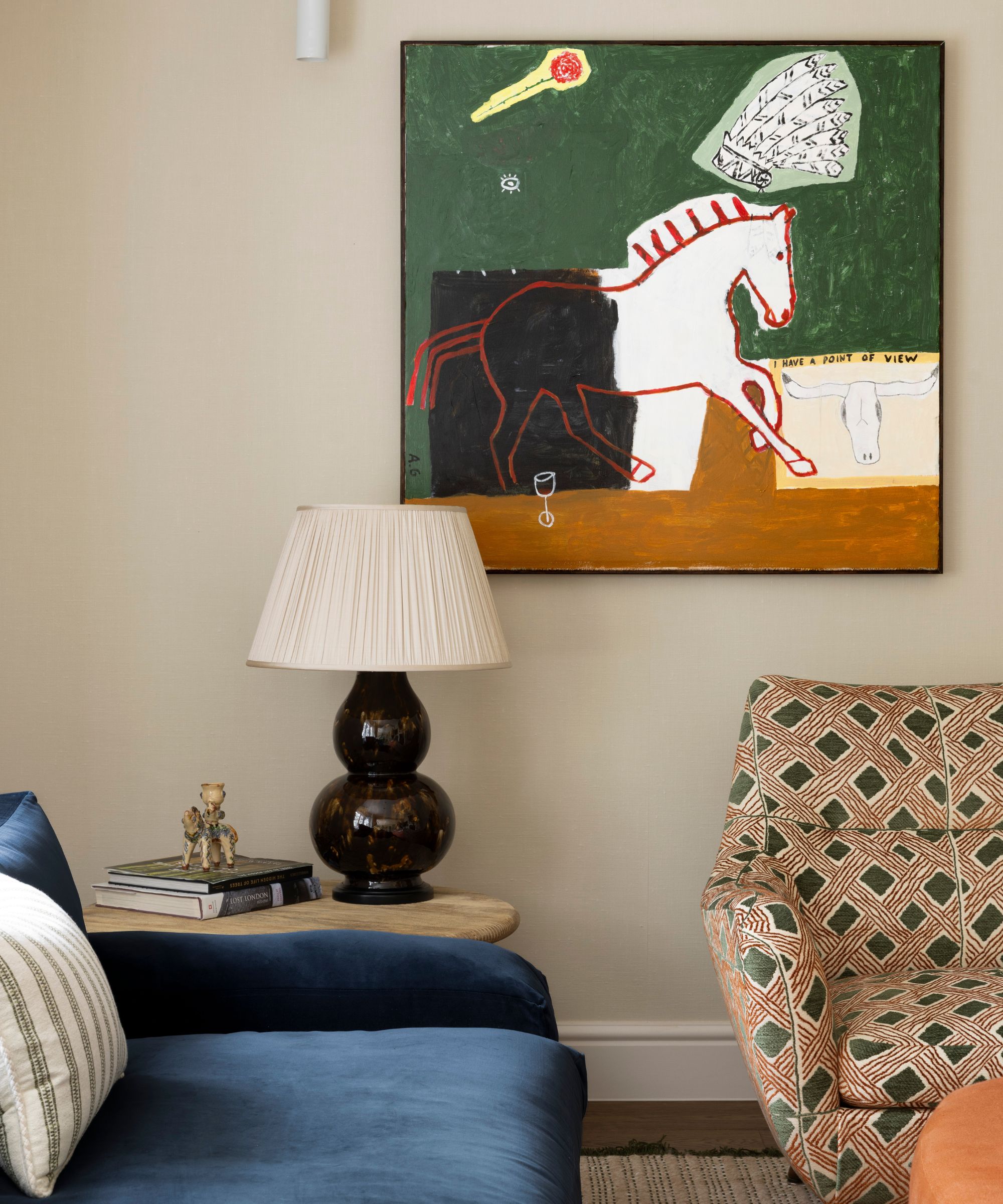 a warm beige sitting area corner with a navy couch, printed armchair and a modern horse painting on the wall