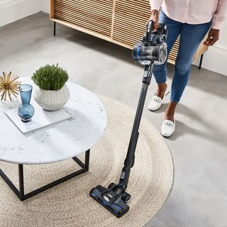 person vacuuming a rug with the Vax ONEPWR Blade 4, in a modern living space with a coffee table