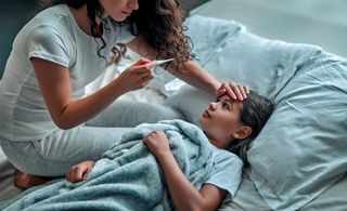 mom takes the temperature of a girl lying down in bed