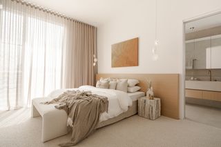 A bedroom in muted tones, opening up to a bathroom in the same materials