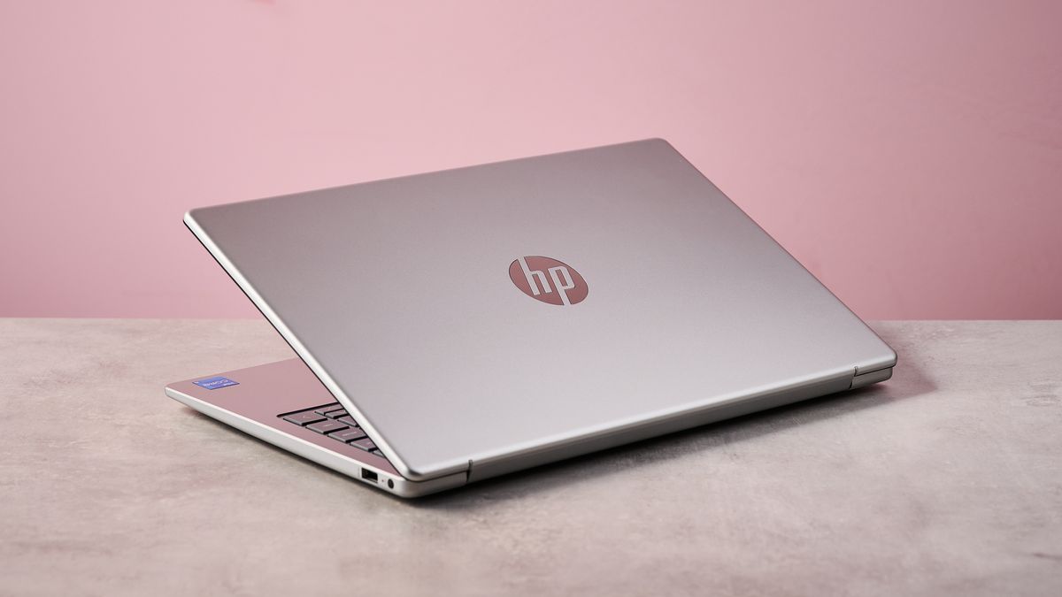 Rear three-quarter view of HP Laptop 14 partially open on white desk with pink wall in background