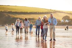 Active Multi-Generation Family With Dog Walking Along Shore On Winter Beach Vacation.