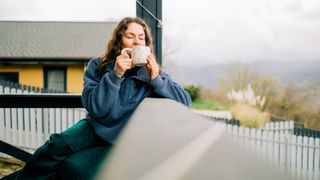 A woman sat on her porch with a morning coffee, enjoying the natural daylight with a countryside landscape in the background