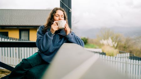 A woman sat on her porch with a morning coffee, enjoying the natural daylight with a countryside landscape in the background