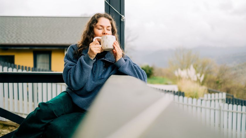 A woman sat on her porch with a morning coffee, enjoying the natural daylight with a countryside landscape in the background
