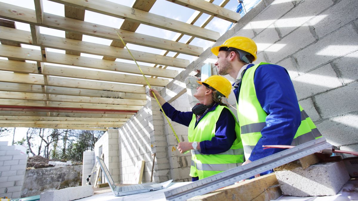 Builders in hi vis jackets and hard hats discussing work plans under timber frames