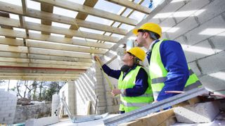 Builders in fluorescent jackets and hard hats measuring under timber frames