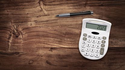 Calculator showing 2023 and a pen on a wooden surface