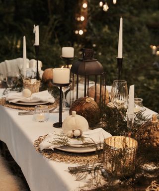 outdoor table scape with thanksgiving theme, white tablecloth, pumpkins, lanterns, candles, greenery