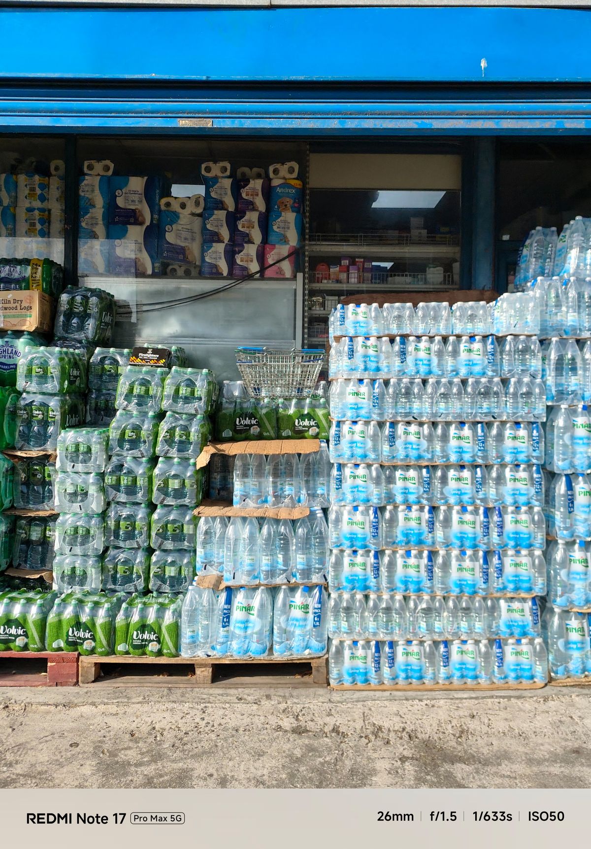 Stacks of bottled water displayed outside a shop beneath a bright blue storefront.