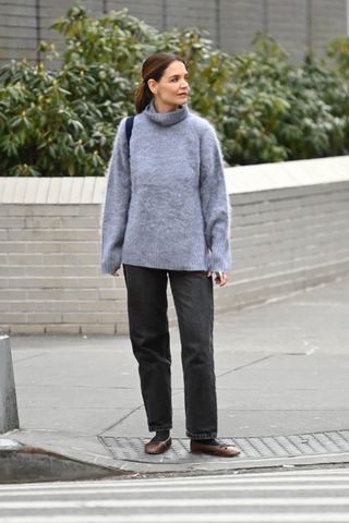 Katie Holmes standing on a street corner wearing a turtleneck sweater with the dark wash denim trend and ballet flats with socks