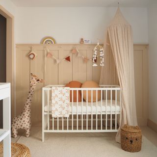 Nursery with panelling wall painted pink, and white cot with canopy above
