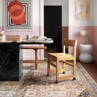 A vintage style rug in pink tones, sitting on top of marble dining table and wooden dining chairs