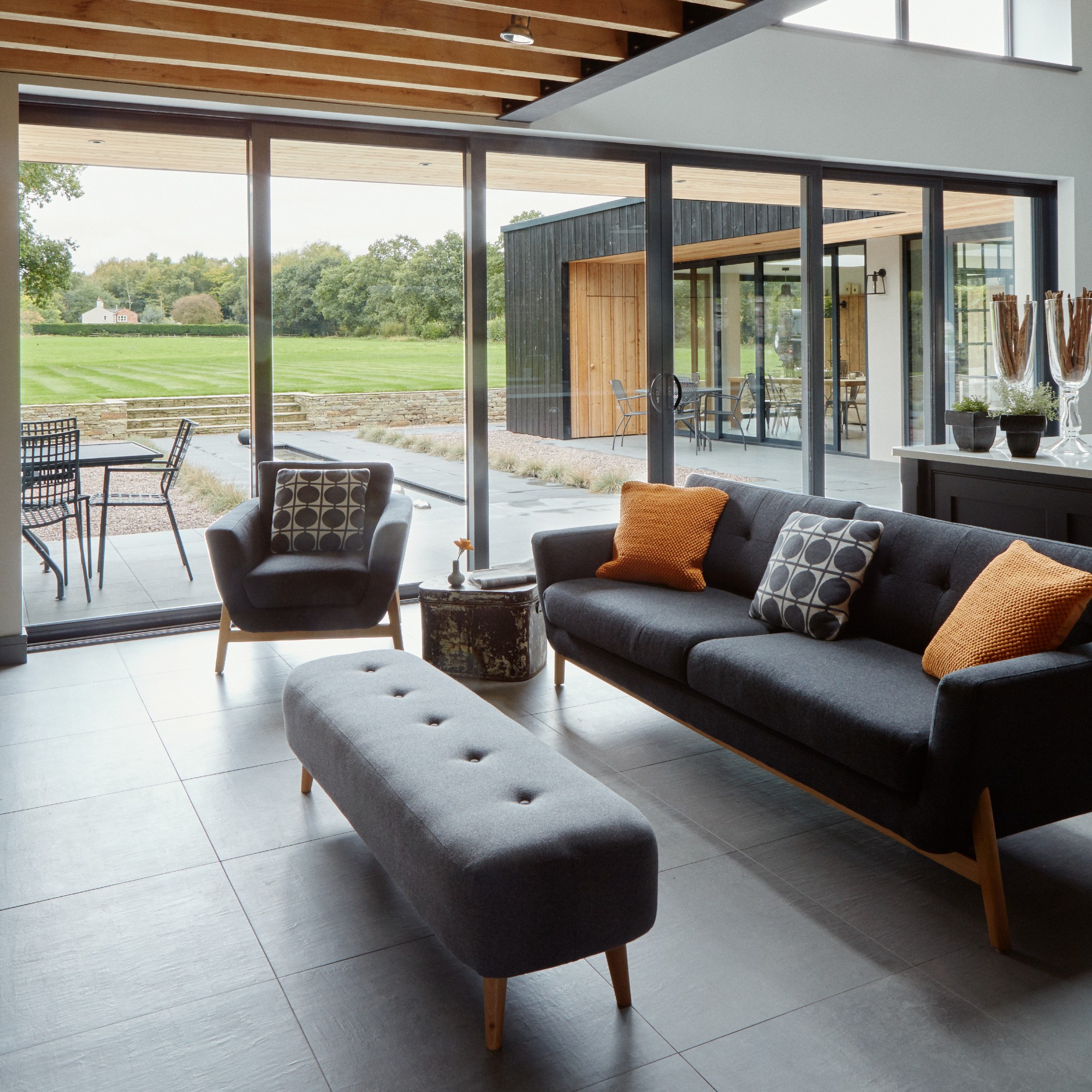 An airy open-plan living room with a dark grey sofa and matching armchair and ottoman
