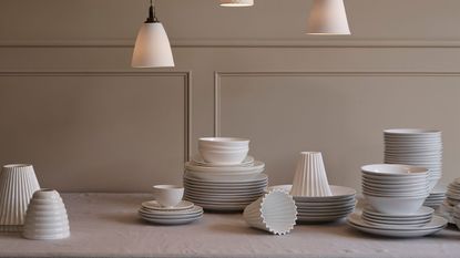 White dinnerware pailed on a table with a white tablecloth, low hanging brass and milk glass pendants above