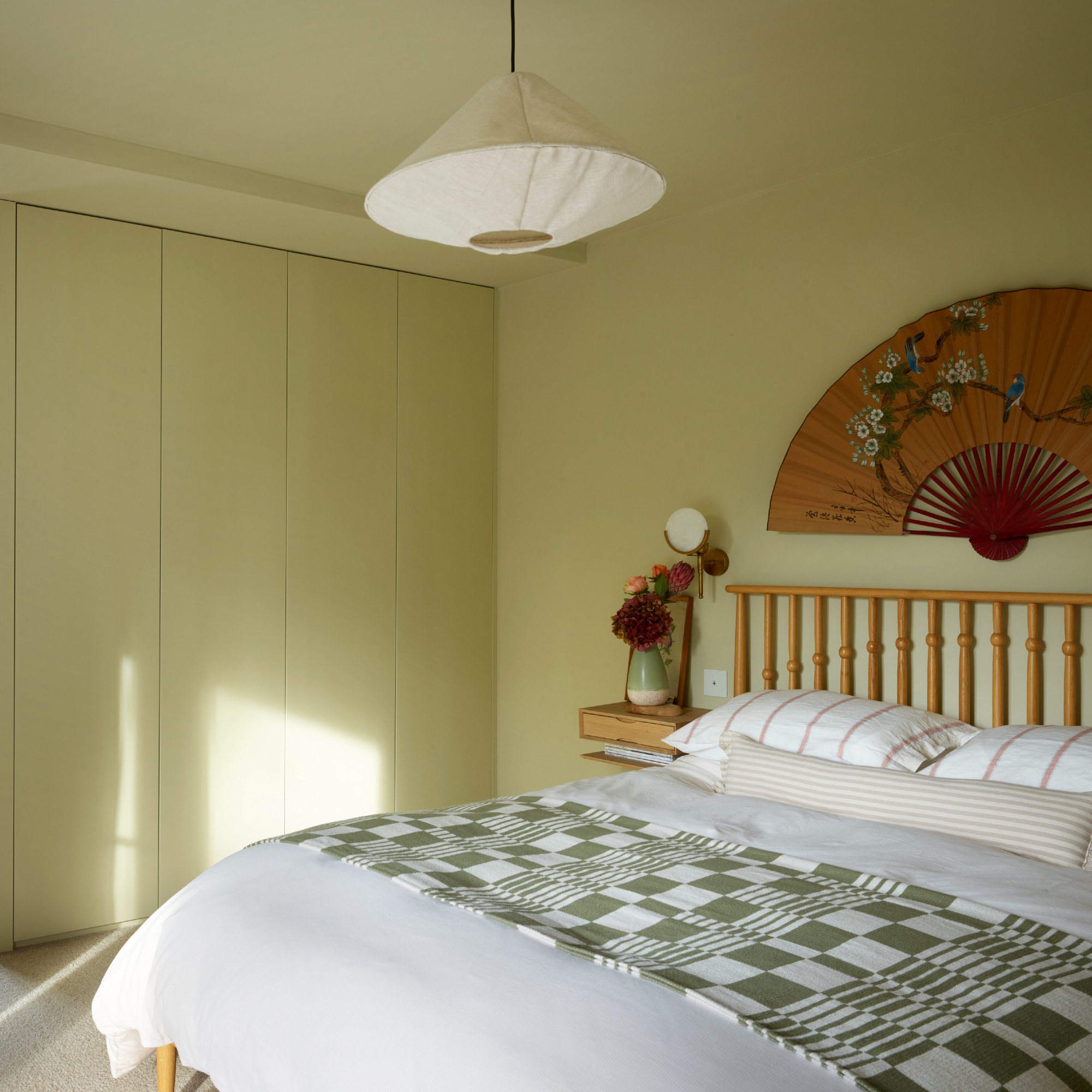 A bedroom colour-drenched in butter yellow with a large fan hung above the bed