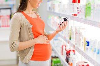 A pregnant woman in a pharmacy reading the label on a bottle.