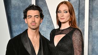 Joe Jonas wearing a black suit jacket and Sophie Turner in a black gown with a cutout neckline on the red carpet for the 2023 Vanity Fair Oscar Party