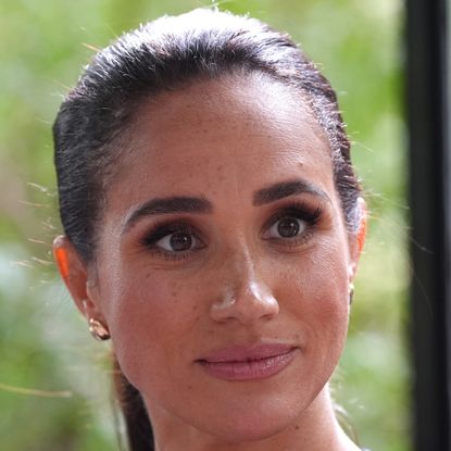 A headshot of Meghan Markle wearing gold earrings, with a serious expression