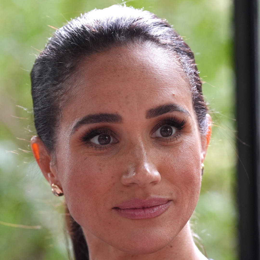 A headshot of Meghan Markle wearing gold earrings, with a serious expression