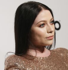 Michelle Trachtenberg wearing a rose gold sequined gown standing in front of a white step and repeat