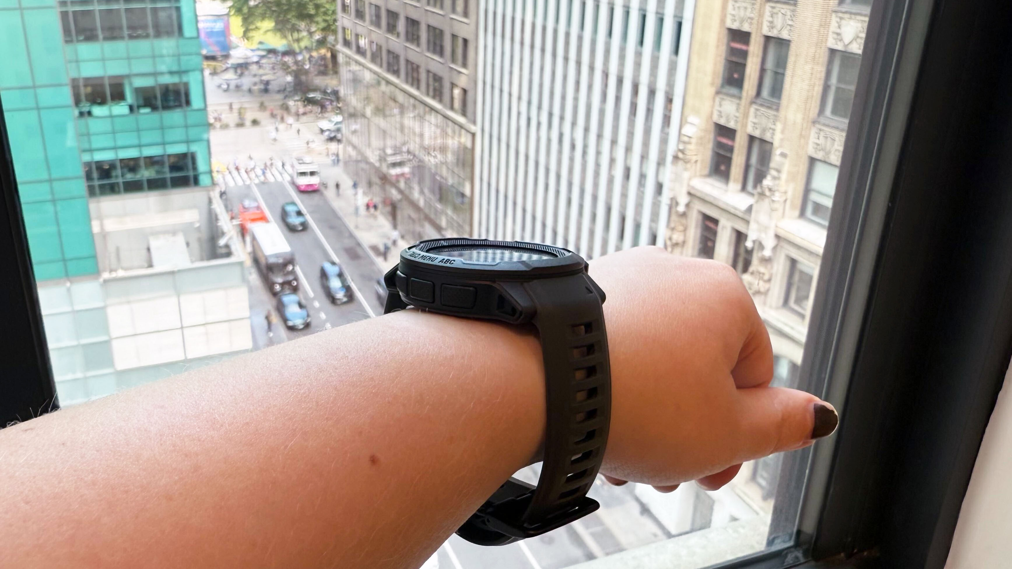 Garmin Instinct 2 Solar on left wrist, in front of a window overlooking Bryant Park in New York City.