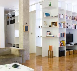 The added element that brings the design together is a white floor-to-ceiling bookshelf complex that characteristically runs through the whole flat, making its appearance in different parts of the house