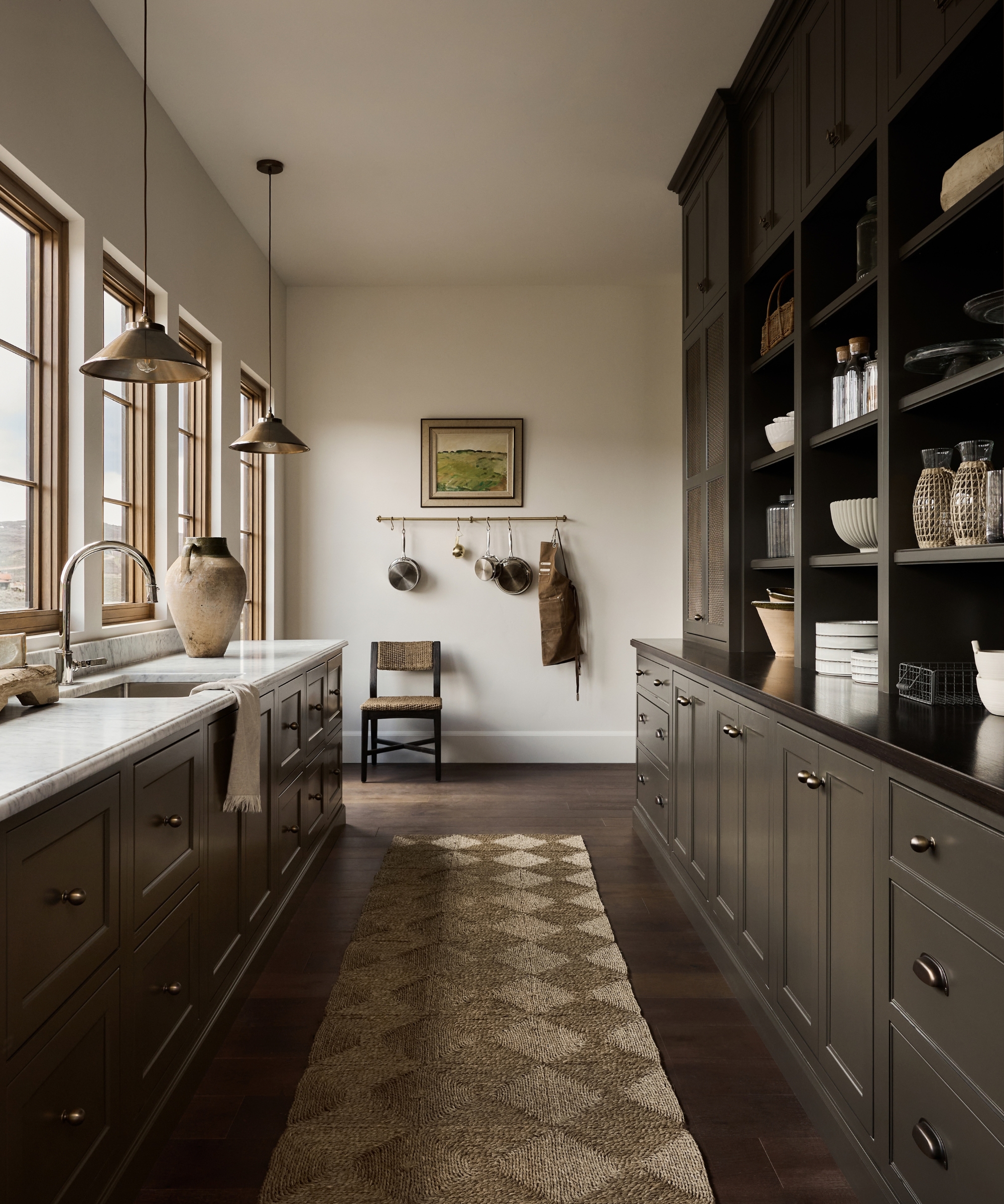 A large pantry with dark brown cabinetry, white walls, and black countertops