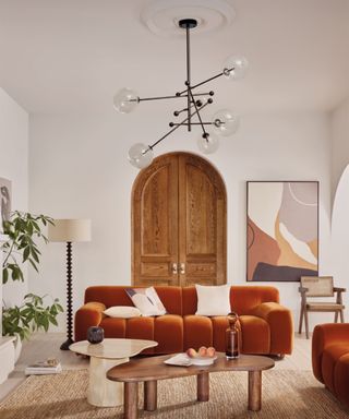rust coloured sofa in cream living room with large pendant light wooden flooring and hessian rug