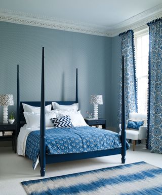 An all blue bedroom scheme with blue four-poster bed, soft furnishings, drapes, rug and wallpaper.