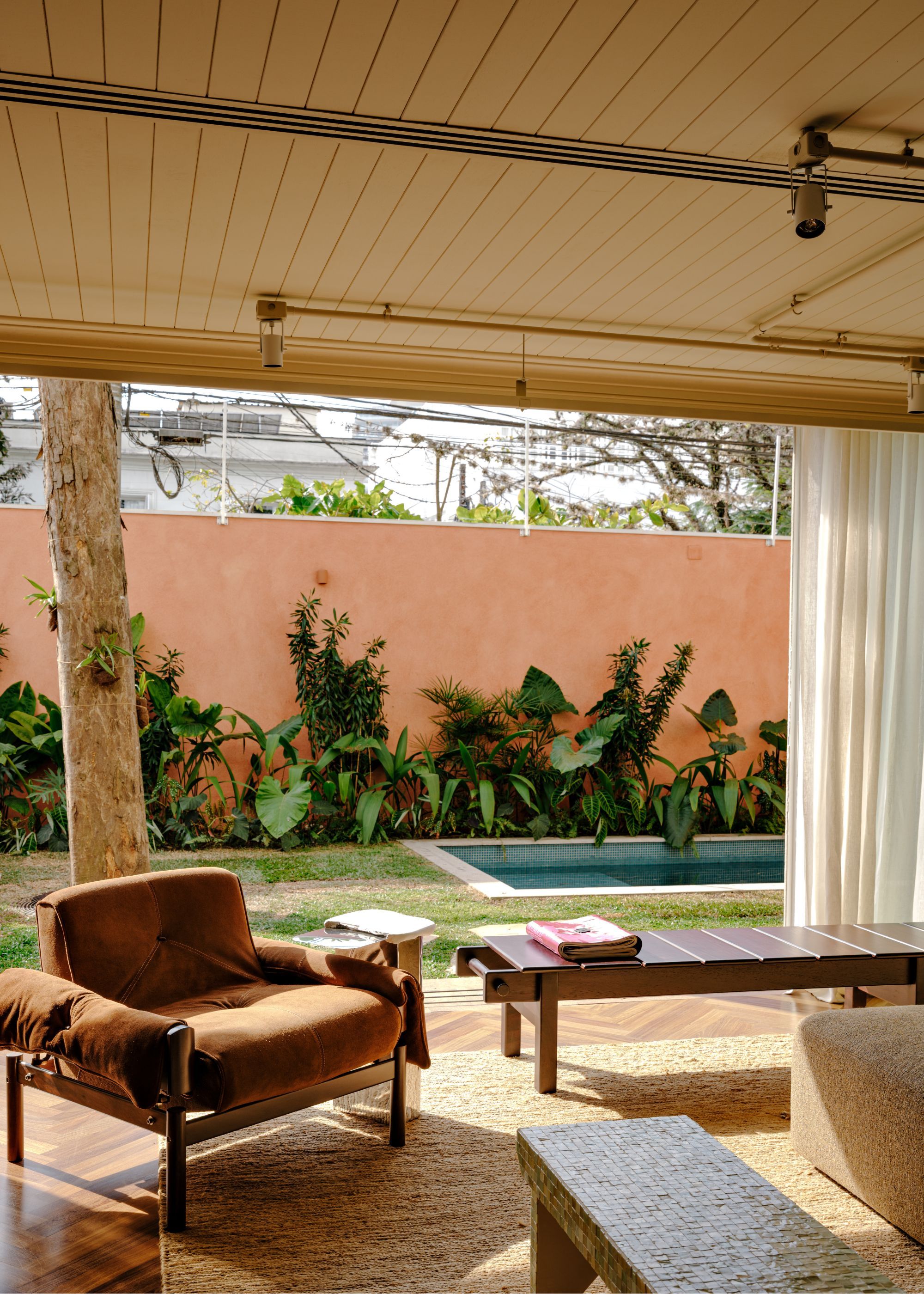 A living room with a low brown chair, natural fibre carpet, a wooden bench, all facing a garden