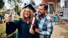Happy graduate and her father taking selfie with smartphone.