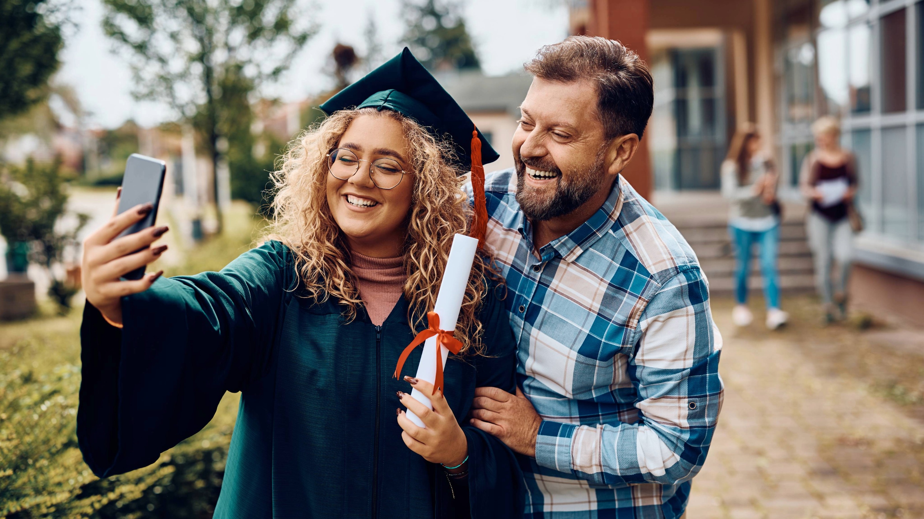 Happy graduate and her father taking selfie with smartphone.