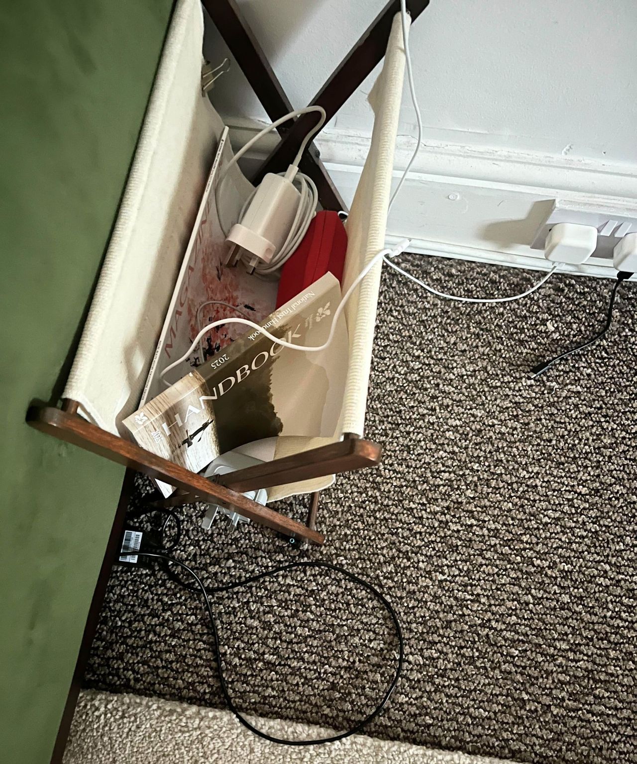 A magazine holder with lots of messy cables in it, some books on top of them.