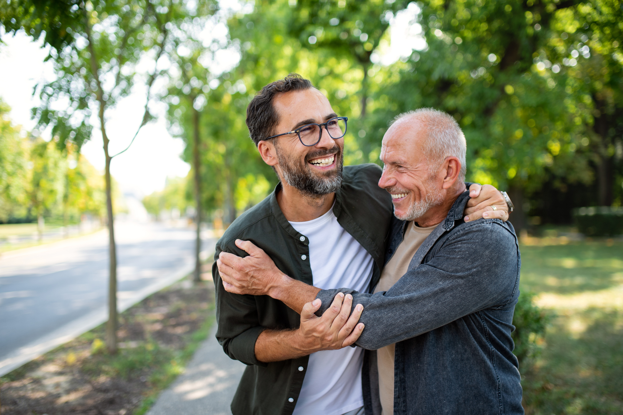 Happy senior father meeting and hugging with his adult son outdoors in park.